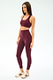 A woman wears the SPLITS59 Sara Airweight Bra in Dark Cherry with high-waisted spandex leggings and beige sneakers, standing against a plain light background.