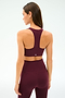 A woman stands with her back to the camera against a plain background, wearing the SPLITS59 Sara Airweight Bra in Dark Cherry and matching high-waisted leggings.