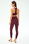 A woman faces away, wearing the SPLITS59 Sara Airweight Bra in Dark Cherry with matching leggings and white sneakers, standing against a plain light background.