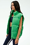 A woman wears the SPLITS59 Summit Nylon Puffer Vest in Grass over a navy sports bra and navy leggings with a white stripe, standing against a plain white background—ideal for cool weather workouts with its lightweight insulation.
