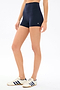Model wears SPLITS59 Airweight High Waist 3.5” Short in Indigo with white sneakers featuring navy stripes, ideal for Pilates or hot yoga, standing against a plain white background.