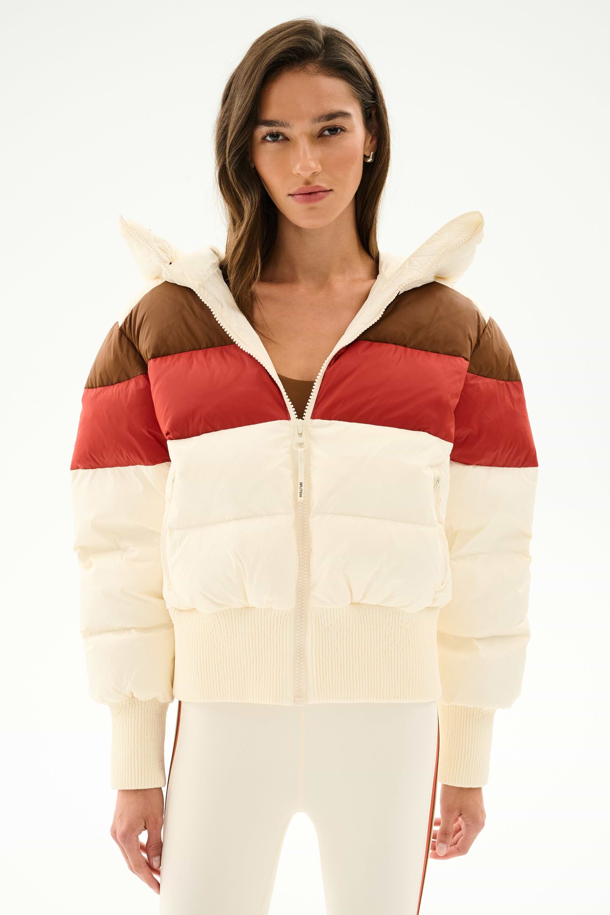 Model wears the SPLITS59 Aspen Puffer Jacket - Creme/Terracotta with cream pants, standing against a plain white backdrop.