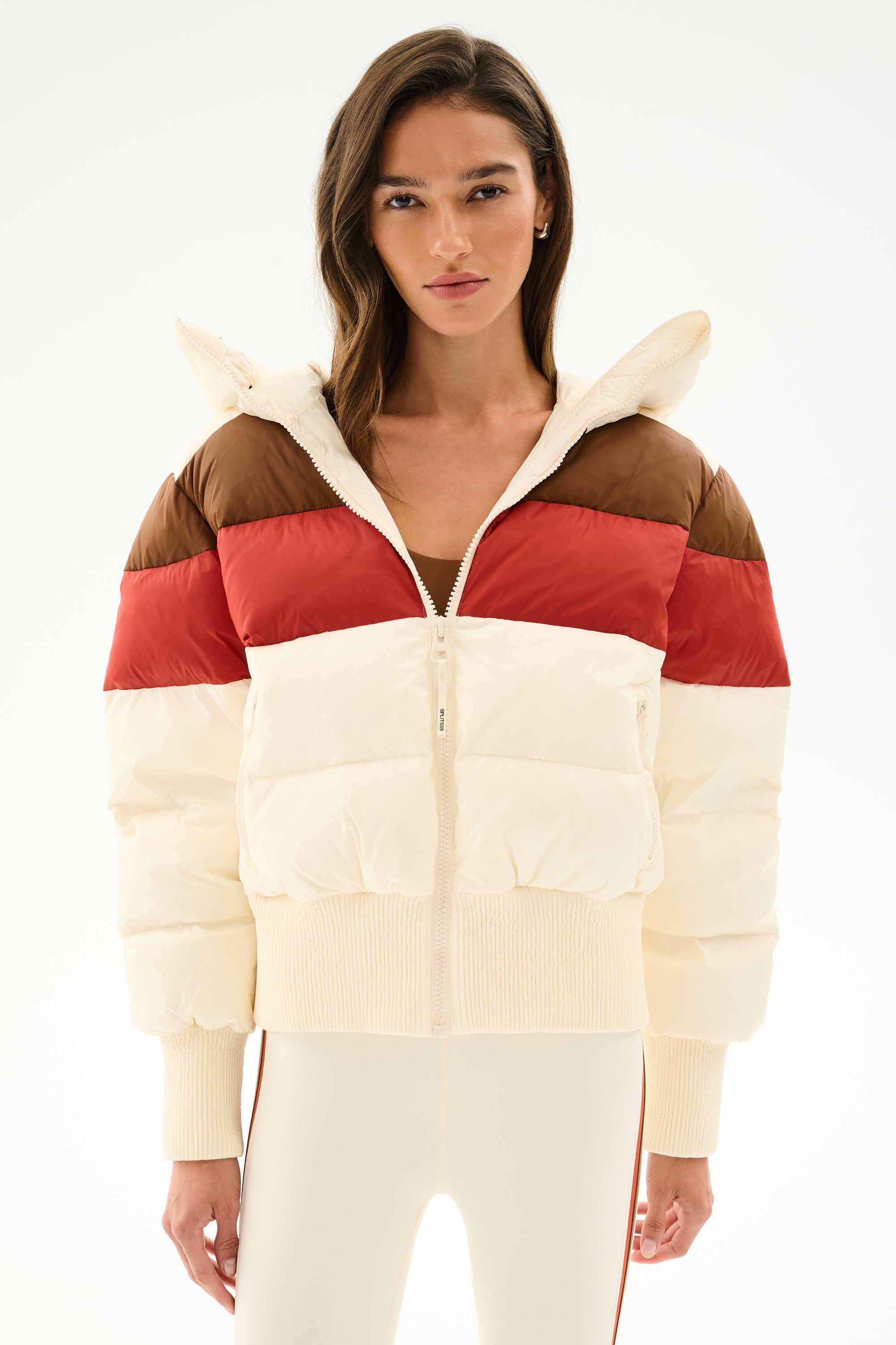 Model wears the SPLITS59 Aspen Puffer Jacket - Creme/Terracotta with cream pants, standing against a plain white backdrop.