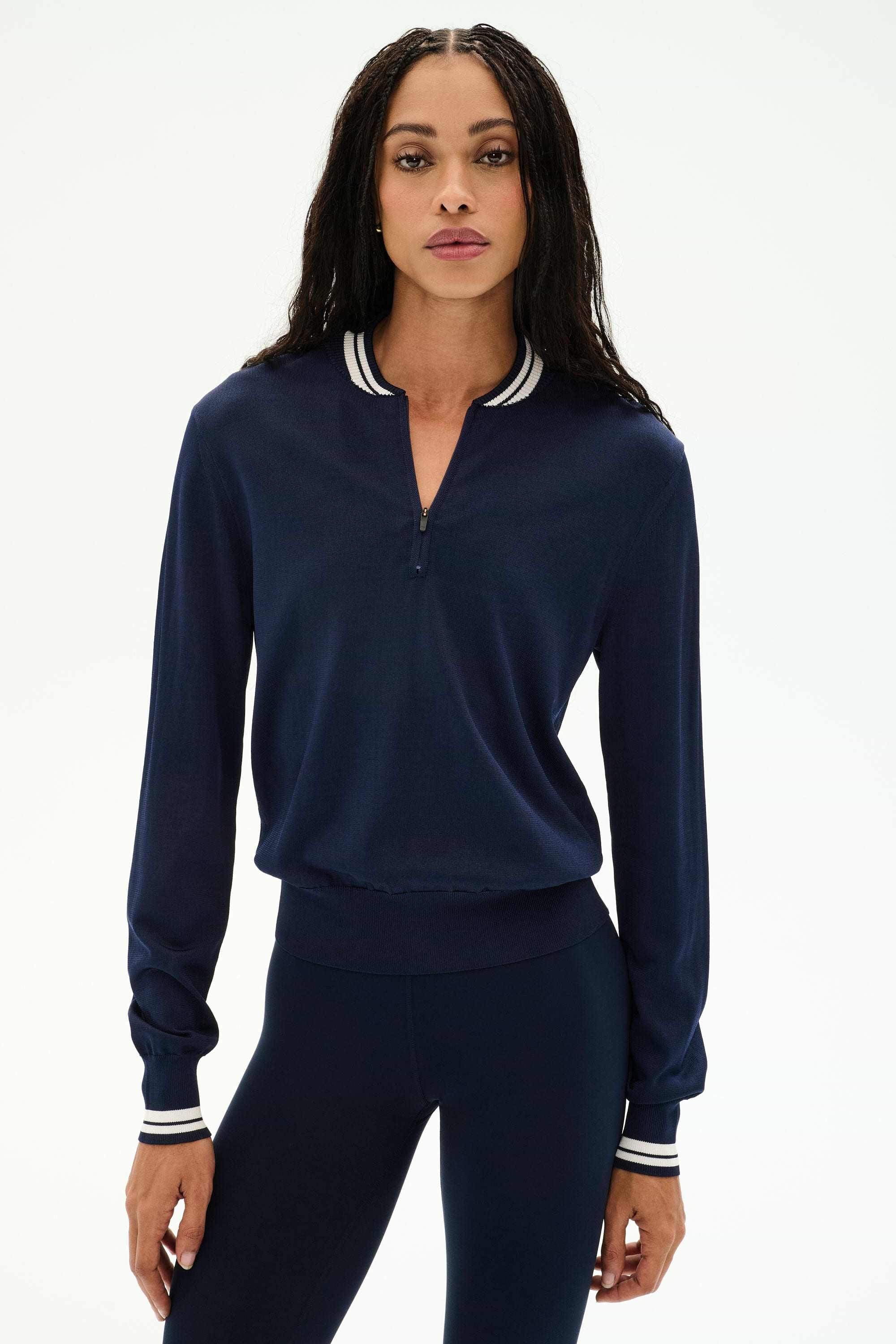 A woman stands facing forward against a plain white background, wearing the SPLITS59 Bonnie Knit Half Zip in Indigo/White—featuring a striped collar and cuffs, crafted from a soft nylon-rayon blend—paired with matching navy leggings.