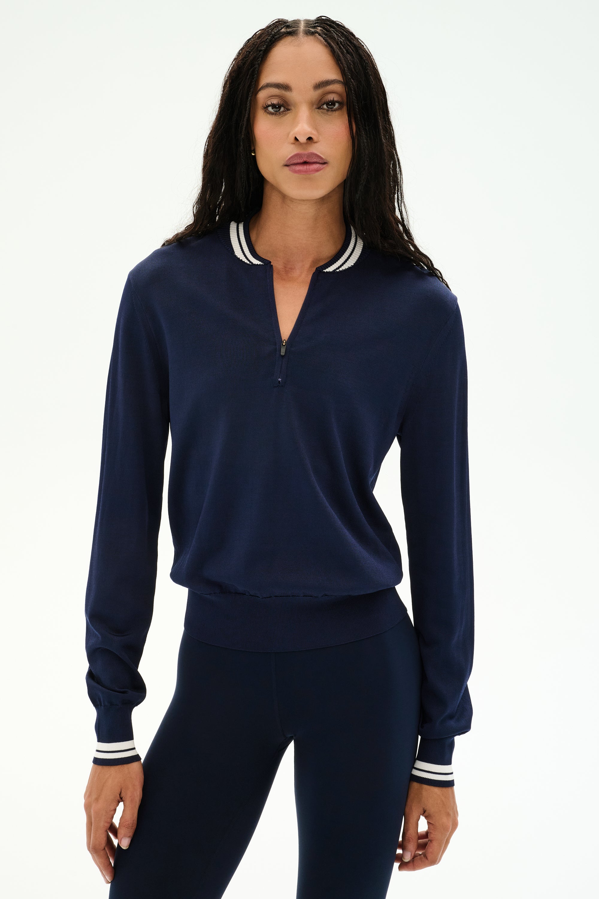 A woman stands facing forward against a plain white background, wearing the SPLITS59 Bonnie Knit Half Zip in Indigo/White—featuring a striped collar and cuffs, crafted from a soft nylon-rayon blend—paired with matching navy leggings.