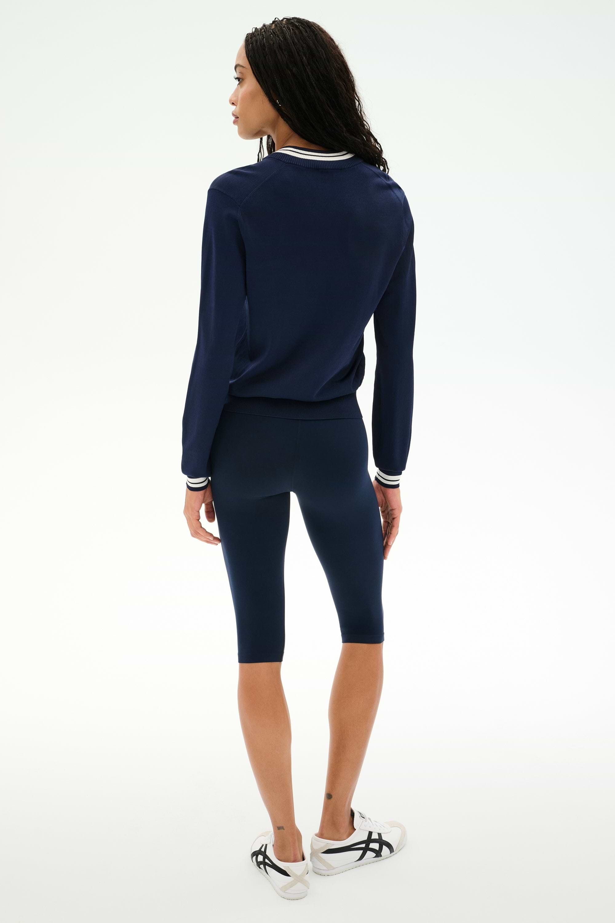 A person stands facing away, wearing the SPLITS59 Bonnie Knit Half Zip in Indigo/White, paired with matching navy knee-length leggings and white sneakers with black accents, against a plain white background.