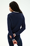 A woman with long dark hair stands with her back to the camera, wearing the SPLITS59 Bonnie Knit Half Zip in Indigo/White—a navy long-sleeve top with white trim—paired with matching navy pants, all crafted from a soft rayon blend.