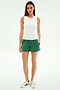 A woman faces forward in a white sleeveless top and SPLITS59 Ella Airweight Track Short in Arugula/White, paired with white sneakers with green stripes, set against a plain white background.