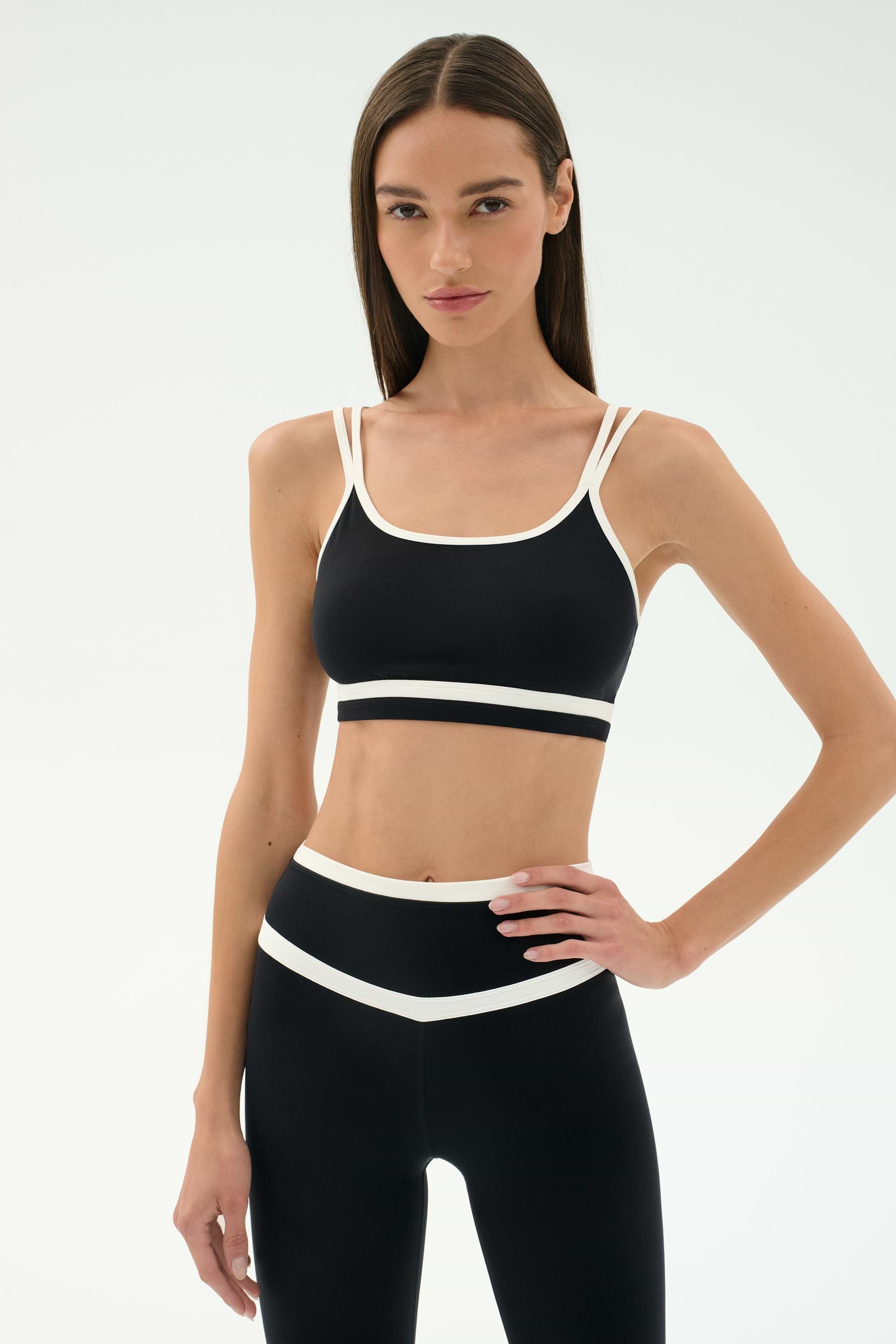 A woman faces forward against a plain light background, wearing the SPLITS59 Eva Rigor Double Strap Bra in black/white and matching leggings.