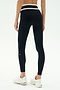 Model wearing SPLITS59 Mason High Waist Rigor Full Length black leggings with a white waistband and white sneakers, standing against a plain light background, facing away from the camera.