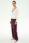 A person is seen standing on a plain white background, wearing the SPLITS59 Jemma Knit V Neck in White/Black—an ultra-soft nylon-rayon blend sweater with black trim—styled with maroon track pants featuring black stripes and white sneakers.