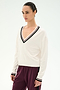 A woman stands against a plain light background wearing the SPLITS59 Jemma Knit V Neck in White/Black—a soft rayon-nylon blend sweater featuring a white V-neck design with black trim—paired with maroon pants.