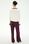 Wearing the SPLITS59 Jemma Knit V Neck in White/Black—a soft rayon blend long-sleeve top with black trim—a person stands facing away against a plain light background, paired with maroon pants featuring a black stripe and black-and-white shoes.