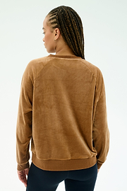 A person with braided hair is seen from the back, wearing the SPLITS59 Joy Velour Crewneck in Honey and dark pants, standing against a plain light background.