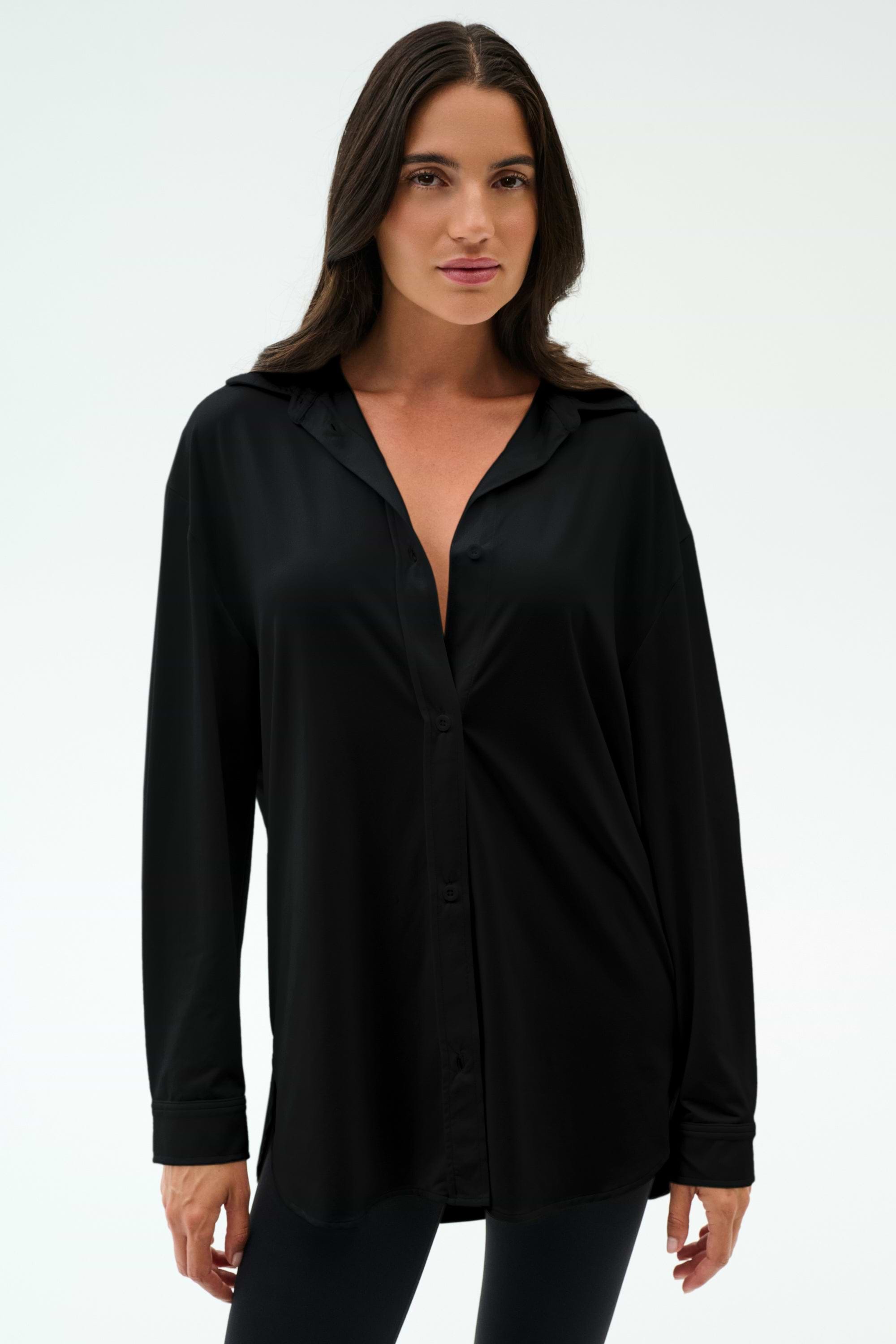 A person stands against a plain background wearing the SPLITS59 Kate Airweight Lite Button Down in black, paired with black pants—a lightweight, minimalist layering essential.