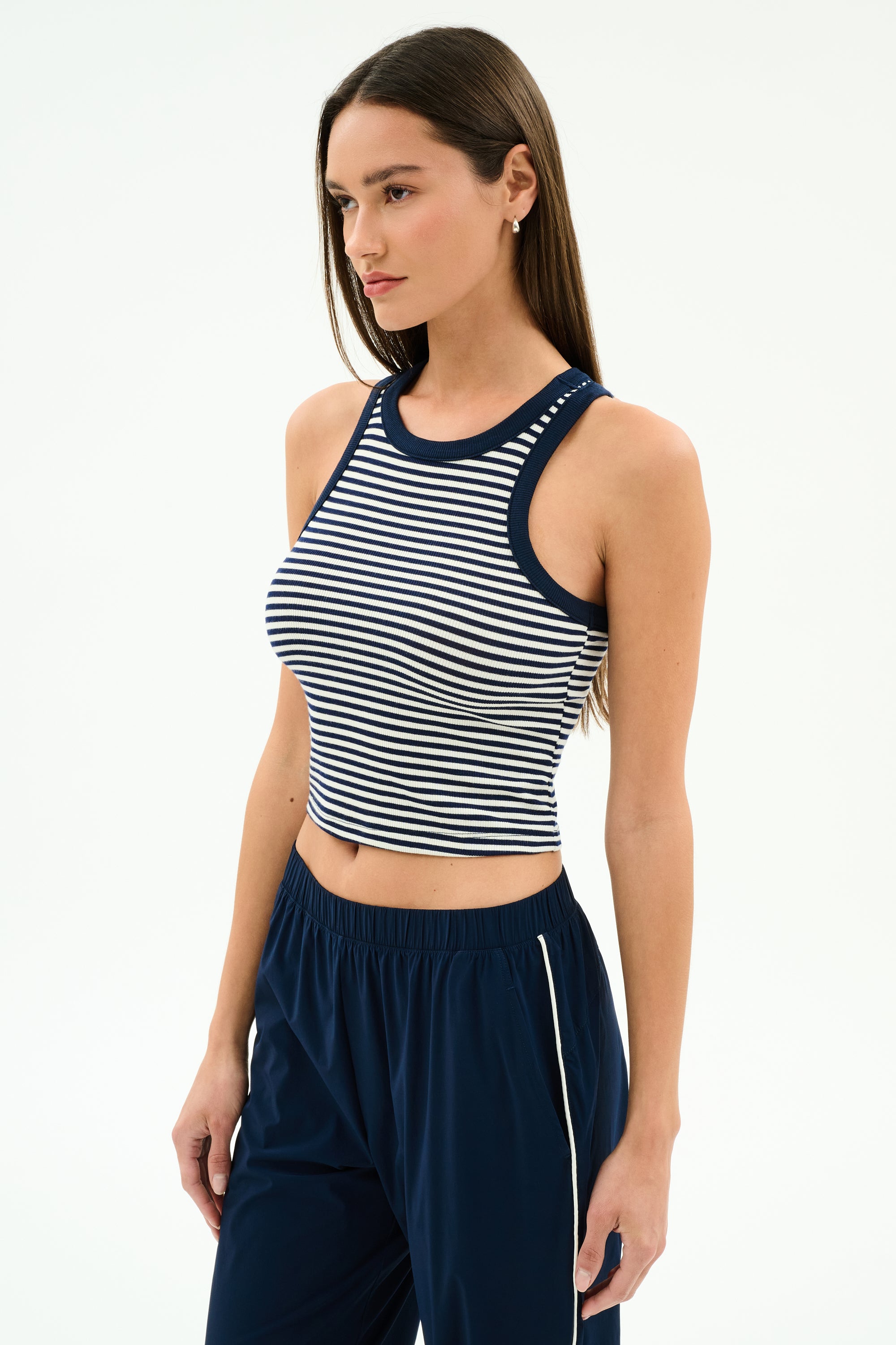 A woman wears the SPLITS59 Kiki Rib Crop Tank in White/Indigo Stripe and navy pants, standing against a plain light background.