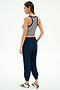 A woman stands against a white background, wearing the SPLITS59 Kiki Rib Crop Tank in White/Indigo Stripe, navy jogger pants, and white sneakers with blue stripes—an ideal gym look—while facing slightly away from the camera.