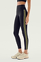 A person wearing the SPLITS59 Margot Rigor Legging in Black/Olive, white athletic shoes, and a black sports bra stands against a plain background.