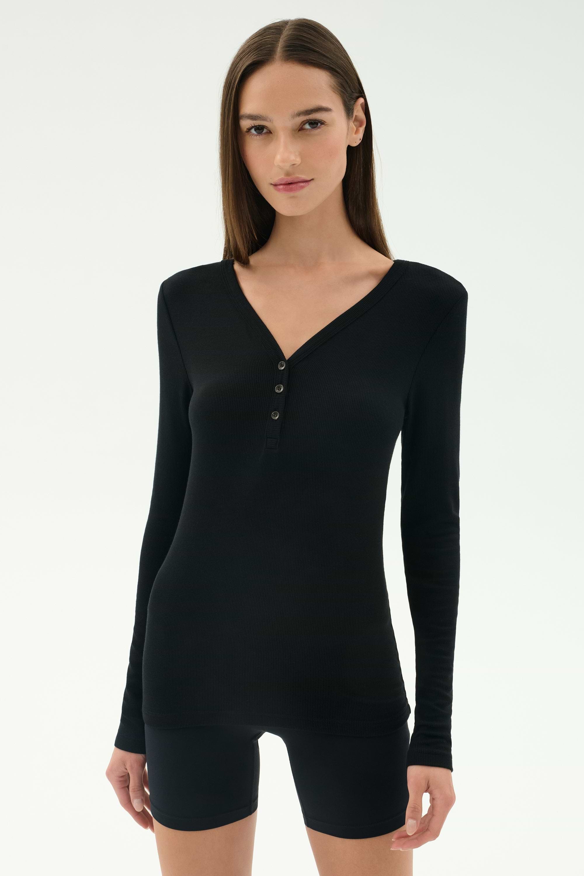 A woman faces forward against a plain light background, wearing the SPLITS59 Louise Rib Henley in black with black shorts.