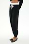 A person wears SPLITS59 Andie Dual Waist Sweatpant in Black/White, featuring a white drawstring and waistband, soft modal blend fabric, paired with a black long-sleeve top and ballet flats, standing against a white background.