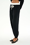 A person wears SPLITS59 Andie Dual Waist Sweatpant in Black/White, featuring a white drawstring and waistband, soft modal blend fabric, paired with a black long-sleeve top and ballet flats, standing against a white background.