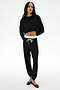 A person stands against a white background wearing the SPLITS59 Andie Dual Waist Sweatpant in Black/White paired with a black cropped sweatshirt and black ballet flats.