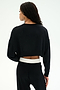 A person with long braided hair faces away from the camera, wearing the SPLITS59 Noah Fleece Crop Sweatshirt in black and matching black pants against a plain white background.