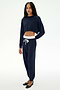 A woman stands against a plain white background wearing the SPLITS59 Andie Dual Waist Sweatpant in Indigo/White and a matching navy blue long-sleeve crop top paired with black flats. This stylish set is proudly made in Los Angeles.