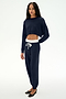 A woman stands against a plain white background wearing the SPLITS59 Andie Dual Waist Sweatpant in Indigo/White and a matching navy blue long-sleeve crop top paired with black flats. This stylish set is proudly made in Los Angeles.