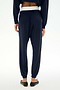 A person stands with their back to the camera on a plain white background, wearing the SPLITS59 Andie Dual Waist Sweatpant in Indigo/White, crafted from ultra-luxe fleece with an exposed white waistband, paired with black ballet flats.