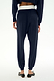 A person stands with their back to the camera on a plain white background, wearing the SPLITS59 Andie Dual Waist Sweatpant in Indigo/White, crafted from ultra-luxe fleece with an exposed white waistband, paired with black ballet flats.