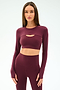 A woman wears the SPLITS59 Amelia Airweight Lite Shrug in Dark Cherry, paired with coordinating leggings, standing against a plain light background.