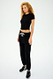 A person with curly hair is wearing a black cropped top paired with SPLITS59 Andie Oversized Fleece Sweatpants in Black, featuring a white drawstring, complemented by black sneakers. They stand against a plain backdrop, ready for cool weather workouts.