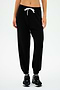 A person donning the SPLITS59 Andie Oversized Fleece Sweatpant in Black, paired with black sneakers and a white crop top, stands against a plain white background. Ideal for cool weather workouts and proudly MADE IN LOS ANGELES.