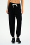 A person donning the SPLITS59 Andie Oversized Fleece Sweatpant in Black, paired with black sneakers and a white crop top, stands against a plain white background. Ideal for cool weather workouts and proudly MADE IN LOS ANGELES.