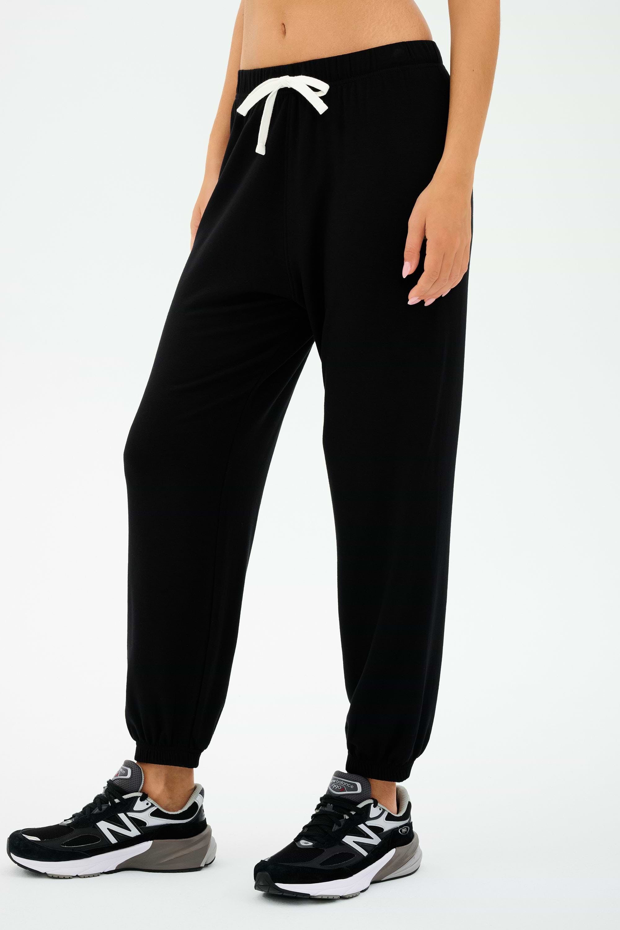 Dressed in SPLITS59's Andie Oversized Fleece Sweatpant - Black with a white drawstring and black sneakers, perfect for cool-weather workouts. Made in Los Angeles, these joggers offer both style and comfort with every step.