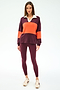 A woman stands against a plain background in the SPLITS59 Katie Fleece Rugby in Dark Cherry/Valencia, paired with maroon leggings and white sneakers.