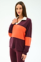 A woman poses against a plain background wearing the SPLITS59 Katie Fleece Rugby in Dark Cherry/Valencia— a long-sleeve maroon and orange color-blocked top—paired with matching maroon pants.