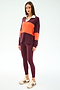 A woman stands against a plain white background wearing the SPLITS59 Katie Fleece Rugby in Dark Cherry/Valencia, maroon leggings, and beige sneakers with maroon stripes.