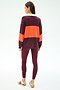 A woman stands facing away, wearing the SPLITS59 Katie Fleece Rugby in Dark Cherry/Valencia with matching maroon spandex leggings and beige sneakers featuring maroon stripes.