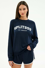 Someone wears the SPLITS59 Andie Oversized Fleece Varsity Graphic Sweatshirt in indigo, featuring "SPLITS59 LOS ANGELES" on the front, paired with matching navy athletic shorts with white trim.