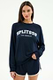 Someone wears the SPLITS59 Andie Oversized Fleece Varsity Graphic Sweatshirt in indigo, featuring "SPLITS59 LOS ANGELES" on the front, paired with matching navy athletic shorts with white trim.