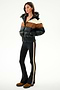 A woman wears the SPLITS59 Aspen Puffer Jacket - Black/Toffee, black flared pants with a tan side stripe, and brown shoes, posed against a plain white background.