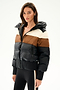 A woman wearing the Aspen Puffer Jacket - Black/Toffee by SPLITS59 and black side-striped leggings stands against a plain white background.
