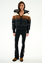 A woman wears the SPLITS59 Aspen Puffer Jacket - Black/Toffee, black flared pants with side stripes, and brown boots against a white background.
