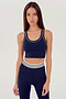 Front view of girl wearing a dark blue ribbed bra that stops at the ribs with thin white line along arms and collar with blue leggings with white and blue waistband