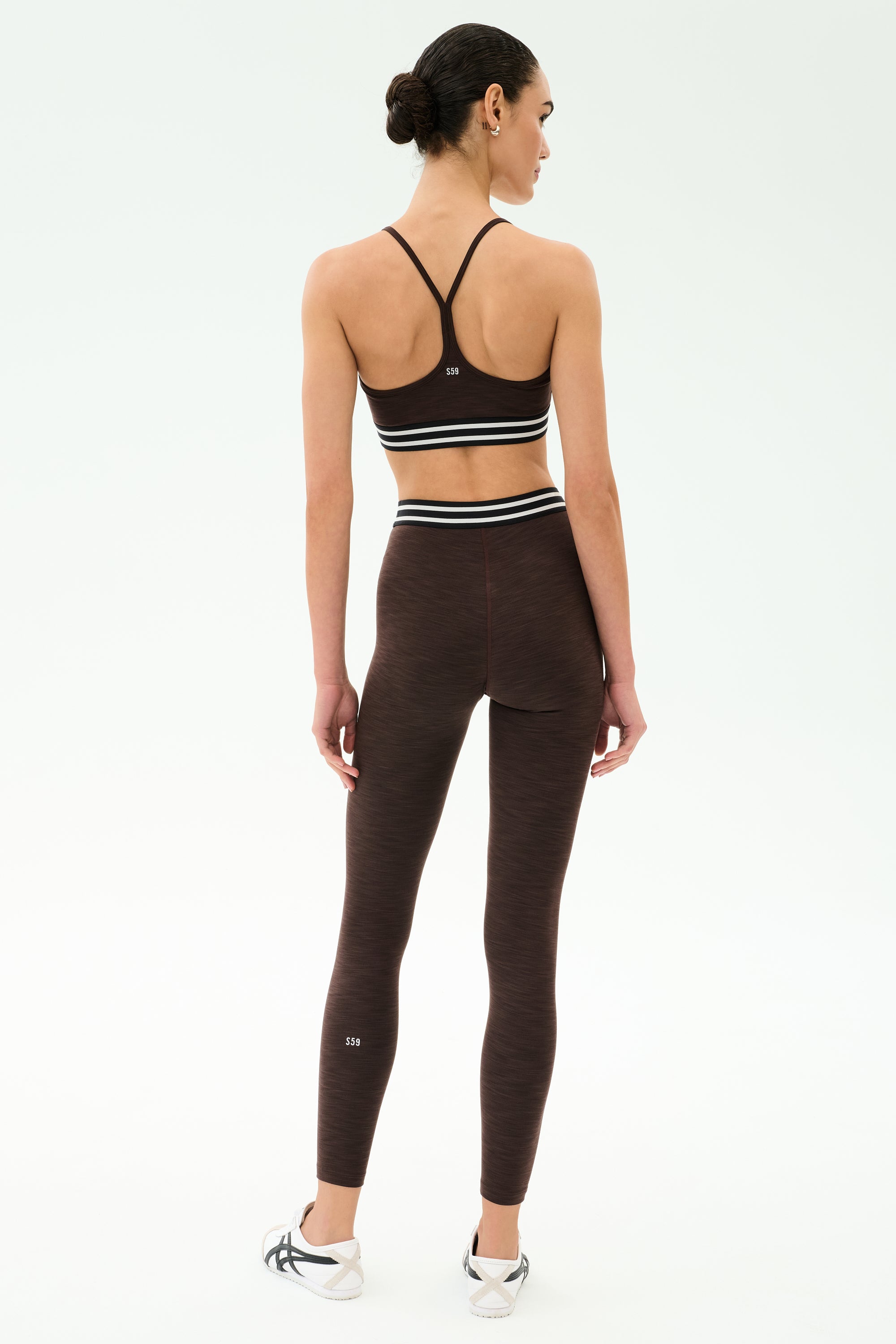 A person wears the SPLITS59 Bailey High Waist Active Rib 7/8 leggings in Heather Dark Chocolate, facing away against a plain light background—ideal activewear for gym workouts.