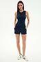 A woman faces forward on a white background, wearing the SPLITS59 Carter Airweight Lite Tank in Indigo with matching navy spandex shorts with pockets and white sneakers featuring navy stripes.