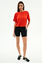 A woman stands against a white background, wearing the SPLITS59 Djuna Oversized Jersey Tee in Lotus Red, paired with black athletic shorts and black sneakers with white stripes—ideal for gym workouts or outdoor activities.