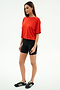 Woman standing against a plain white background, wearing the SPLITS59 Djuna Oversized Jersey Tee in Lotus Red, black bike shorts, and black Adidas sneakers—ideal for gym or outdoor workouts.